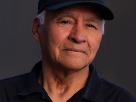 Man wearing a dark blue polo shirt, his silver sideburns can be seen under a dark blue baseball cap.