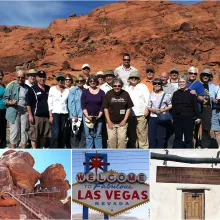 group of people smiling at the camera, standing in front of a red rock formation in the Mojave Desert.